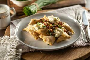 Fried pierogi served on a plate with bryndza cheese, bacon, and chives photo