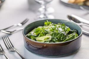 Kohlrabi and spinach leaves salad in a dark bowl in the restaurant photo