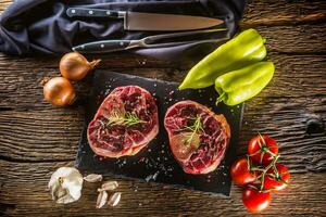 Two pieces raw beef shank and basic ingredients on goulash - onion pepper tomatoes garlic salt spices and rosemary photo