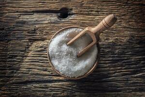 Coarse-grained salt in a wooden bowl with a ladle on an old oak table photo