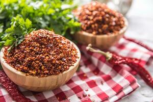 Dried and crushed chili peppers in wooden bowles with parsley herbs photo