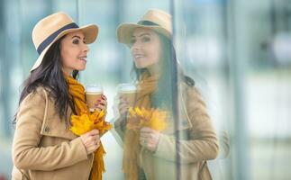 Young fashionable woman is doing window shopping holding takeaway coffee and autumn leaves photo