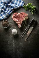 Rib eye steak with bone on butcher board with herbs salt pepper fork and knife photo