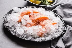 en porciones crudo salmón filetes en hielo en plato con limón y Romero foto