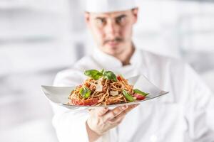 Chef in restaurant kitchen holding plate with italian meal spaghetti bolognese photo