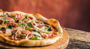 Italian pizza with prosciutto tomatoes olives olive oil parmesan cheese and arugula. photo