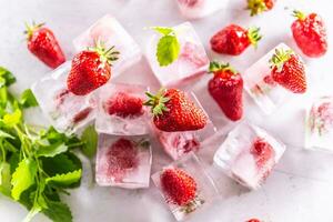 Strawberries frozen in ice cubes with mellisa leaves - Top of view. photo