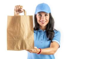 Young dark-haired employee holding a paper takeaway bag in front of her ready for the customer. Isolated background photo