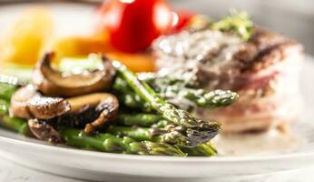 Grilled steak served on a plate with asparagus, mushrooms and sauce photo