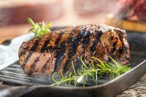 Grilled beef steak in grill pan with herbs rosemary on wooden table photo