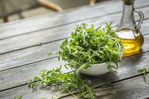 Fresco Rúcula ensalada con aceituna petróleo en blanco plato en de madera mesa foto