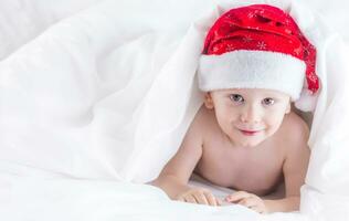 Cute baby boy with santa hat on bed under white duvet photo