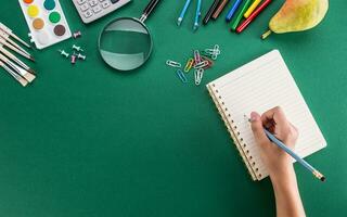 estudiante de el niña mano desde un lápiz con cuaderno y colegio suministros foto