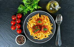 Homemade meatballs with tomato sauce and spices served in black pan on black slate background photo