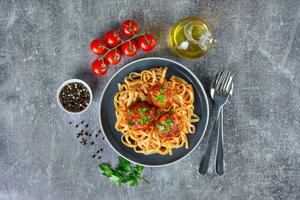 Homemade meatballs with tomato sauce and spices served in black pan on gray concrete background photo