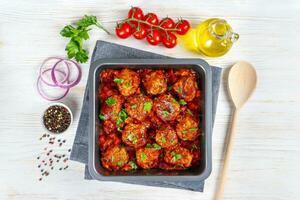 Homemade meatballs with tomato sauce and spices served in black pan on white wooden background photo