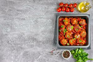 Homemade meatballs with tomato sauce and spices served in black pan on grey concrete background photo