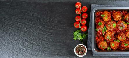 Homemade meatballs with tomato sauce and spices served in black pan on black slate background photo