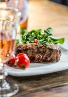 Beef Steak. Juicy beef steak. Gourmet steak with vegetables and glass of rose wine on wooden table photo