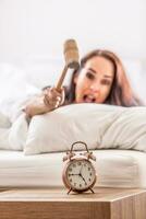 Smashing of alarm clock with the hammer by a woman reaching out from the bed photo