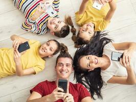 Parents and three children all hold mobile phones in their hands looking up photo