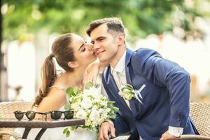 Loving bride kissing her charming huband. They wear wedding robes and hold beautiful bouquet photo