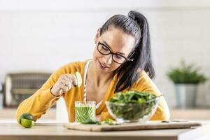 A smiling brunette is preparing a spinach smoothie and flavoring it with lime juice photo