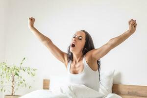 Woman stretches her arms wide open and yawns as she wakes up in the morning in the bed photo