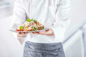 Chef in restaurant kitchen holding plate with italian meal spaghetti bolognese photo