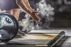 Muscular weightlifter clapping hands before barbell workout at the gym with dumbbells photo