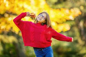 contento otoño niña sonriente y alegre participación otoño hojas. hermosa joven niña con arce hojas en rojo cárdigan foto