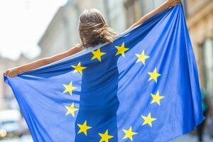 UE bandera. linda contento niña con el bandera de el europeo Unión. joven Adolescente niña ondulación con el europeo Unión bandera en el ciudad foto