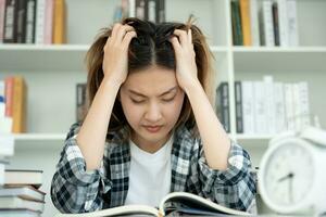 Asian student woman have anxiety because of exams, female prepare for test and learning lessons in the library. stress, despair, haste, misunderstanding reading, discouraged, expectation, knowledge photo