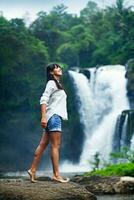 a woman standing on a rock near a waterfall photo