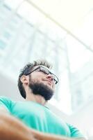 un hombre con lentes y un barba en pie en frente de un edificio foto