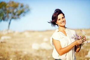 a woman is standing in a field holding a bunch of flowers photo