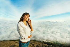 a woman talking on a cell phone while standing on a mountain photo