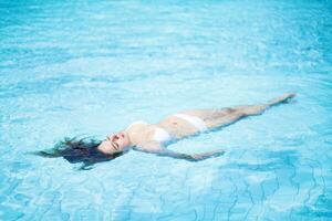 a woman in a white bikini floating in a pool photo