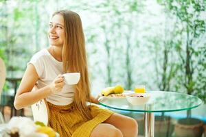 un mujer sentado a un mesa con un taza de café y Fruta foto