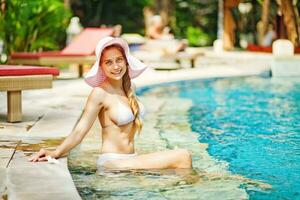 a woman in a bikini sitting by a swimming pool photo