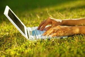 a person typing on a laptop in the grass photo