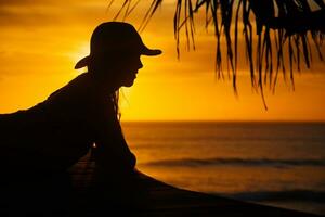 un mujer en un sombrero sentado en un muelle a puesta de sol foto