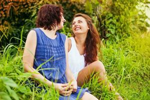 mother with grown up daughter sitting on a grass and affectionately talking photo