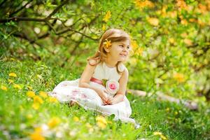 un pequeño niña sentado en el césped con flores foto