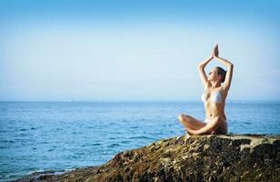 un mujer en un bikini es haciendo yoga en un rock por el Oceano foto