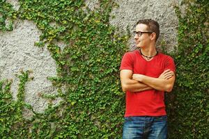 a man in a red shirt and glasses standing in front of a wall covered in ivy photo