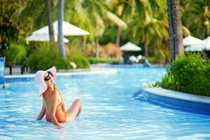 un mujer en un sombrero y naranja traje de baño en un piscina foto