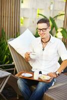 un hombre sentado en un silla participación un bandeja con un taza de café foto