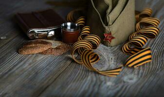 Military cap, carnations, Saint George ribbons, flask with alcohol  on a wooden surface. photo