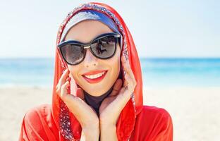 beautiful muslim caucasian russian woman wearing red dress relaxing on a beach photo